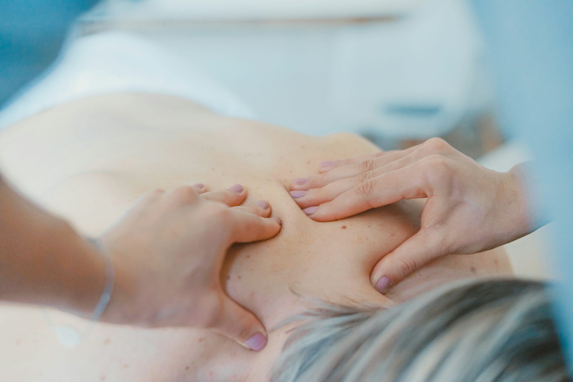 Schmerztherapie Zwei Hände massieren den Nacken einer Person auf einer Liege.